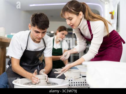 Young woman and young man sculpting product on potter's wheel Stock Photo