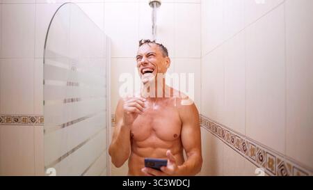 Man laughing while using smartphone in shower Stock Photo