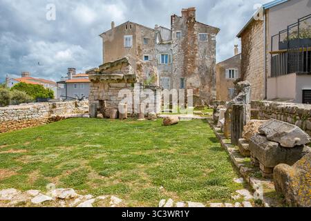 Ancient Roman ruins with broken columns and stone walls in the historic center of Porec, Istria, Croatia. Weathered buildings in the background add to Stock Photo