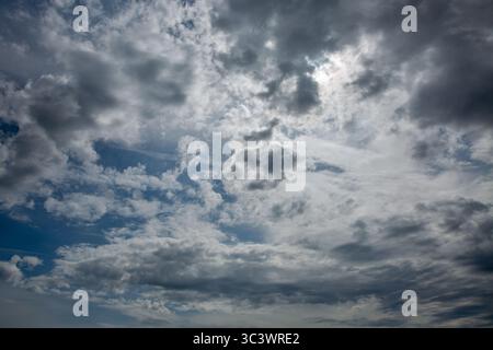 Dynamic cloudscape with swirling grey and white storm clouds creating dramatic patterns across overcast sky. Perfect atmospheric background for weathe Stock Photo