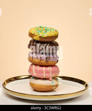 Stack of donuts with different toppings and glazes on round plate, beige background Stock Photo