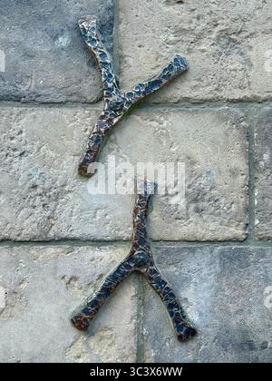 Close-up of two decorative Y-shaped metal branches attached to a textured stone wall. The metallic elements feature a patterned surface, contrasting w Stock Photo