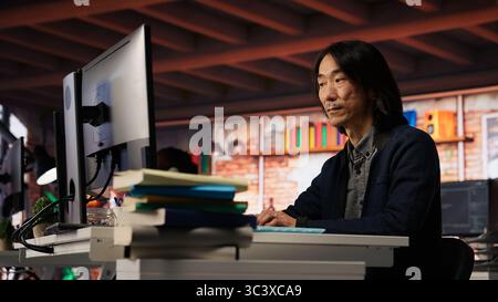 Startup manager leveraging machine learning technology in office to gain competitive edge. Asian Silicon Valley company IT expert working on rapid technological advancement, camera B Stock Photo