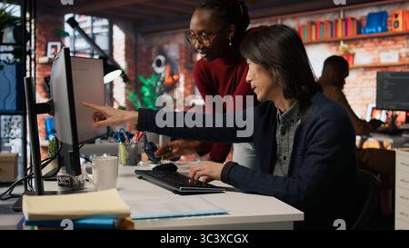 AI startup office admin asks questions to senior team leader before starting implementing machine learning. Tech venture company worker requests help from manager to fix code bugs, camera A Stock Photo