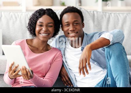 Black couple with cleaning tools resting, using digital tablet Stock Photo