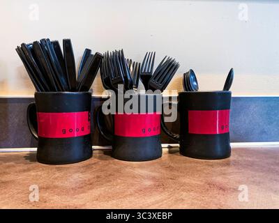 Three mugs holding black plastic forks, spoons and knifes for self service by customers. Stock Photo