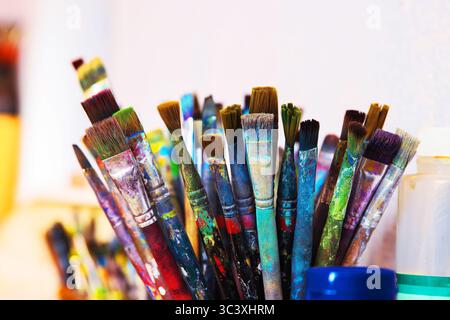 A cluster of well used paintbrushes with colorful dried paint on their handles and bristles in container in creative art studio. Stock Photo