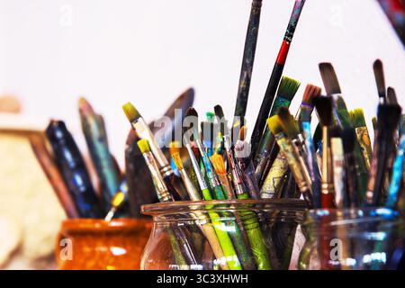 A collection of used paintbrushes varied with colorful stains  in glass and ceramic jars, arranged on a work table in an art studio. Stock Photo