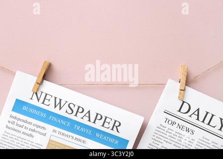 Different newspapers hanging on rope against pink background Stock Photo