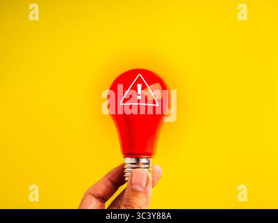 dangerous ideas, scam beware, phishing, social media and internet security, data protection concept. Warning sign on red light bulb, holding by human Stock Photo