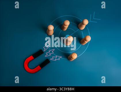 Digital marketing, target audience, Customer attraction concept. Big horseshoe magnet attracting wooden figure group on target icon, blue background. Stock Photo