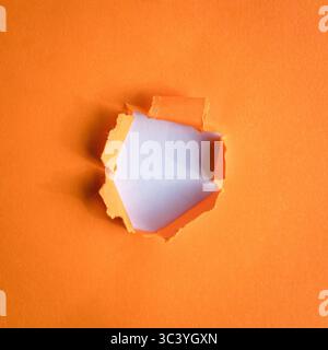 Round hole ripped in orange paper on white background. Copy space. Stock Photo