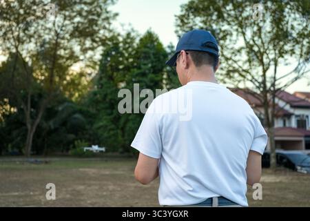Man operating drone with controller standing with back on a field. Stock Photo
