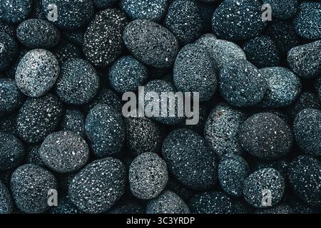 Close-up of dark volcanic pebbles with speckled texture. Natural pattern of rounded black stones, densely packed and detailed. Ideal for background or Stock Photo
