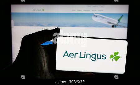 Stuttgart, Germany - 06-11-2025: Person holding mobile phone with logo of Irish airline company Aer Lingus on screen in front of web page. Stock Photo