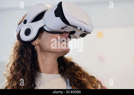 Woman wearing wireless VR headset looking upward in white minimalist room with blurred shapes Stock Photo