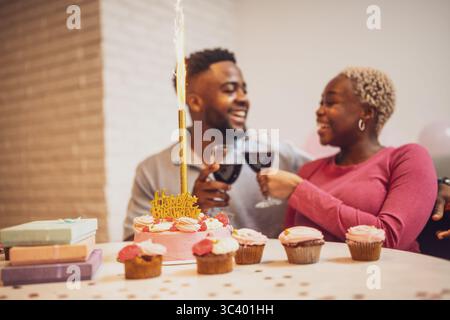 Happy young couple celebrating woman's birthday at home. They are toasting with wine. Stock Photo