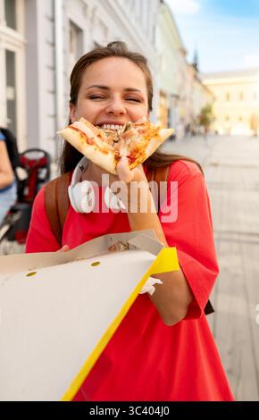 Happy female student eating pizza on city street Stock Photo