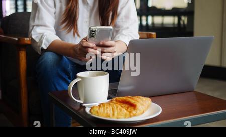 front view of woman using phone and laptop computer at home or coffee shop for work in the morning with hot coffee, anonymous face. working from home Stock Photo