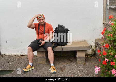 Tired hiker and photographer taking a break on a concrete bench next to blooming flowers Stock Photo