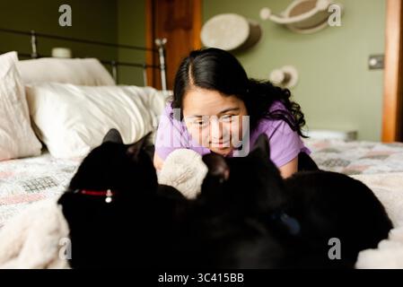 Young woman with down syndrome playing with black cats on bed Stock Photo