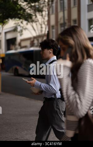 Young man walking in city with food and wireless earbuds Stock Photo