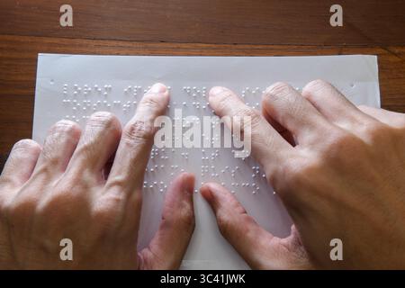 Visually impaired individuals use their fingertips to perceive Braille on paper, allowing them to read. Text on the paper is a dummy Lorem ipsum text. Stock Photo