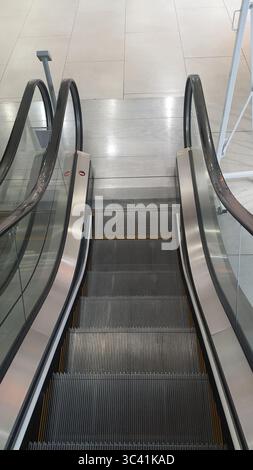 Modern escalator moving downwards in a spacious shopping mall or airport, featuring sleek metal and glass sides, creating a bright and clean atmospher Stock Photo