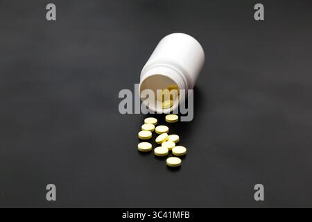 White plastic jar on a black background with poured pills. Stock Photo