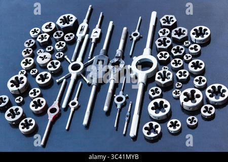 A lot of dies and holders for them of different sizes for threading in metal, on a black background. Stock Photo