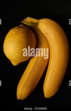 Still Life Photograph of Fresh Yellow Bananas and Lemon on a Black Background Stock Photo