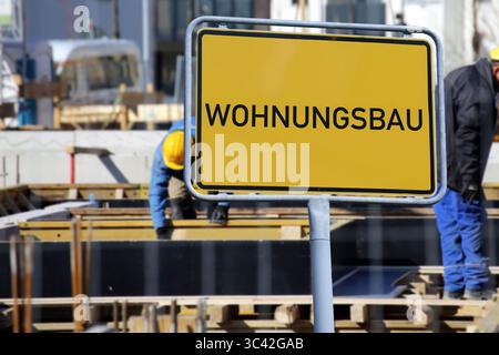 (Photo montage) Town sign with the inscription WOHNUNGSBAU (housing construction) in front of workers on a construction site Stock Photo