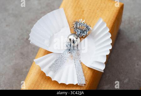 The angel is made out of cupcake wrappers and has a silver bell on its head. The angel is decorated with silver ribbons, giving it a festive Stock Photo