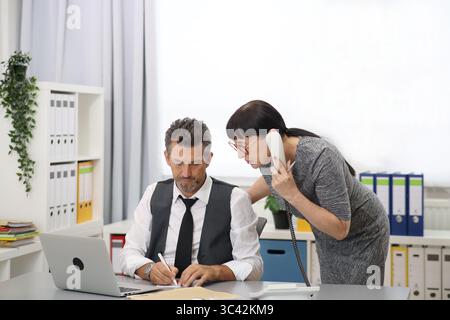 Man writes, woman talks on the phone in the office Stock Photo