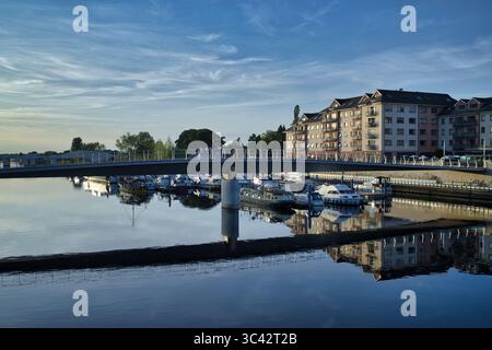 A serene waterfront scene in Ireland, featuring a bridge over calm water with reflections of boats and buildings. Stock Photo