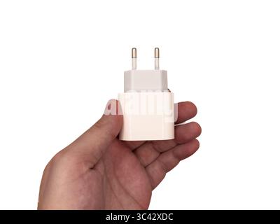 Phone charger, USB type c charger, white charger/ A hand holding a white charger. The charger has two prongs and is plugged into a wall outlet Stock Photo