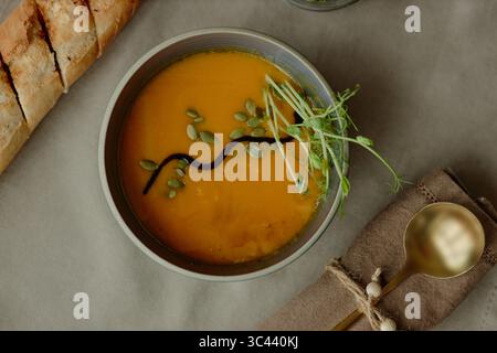 Bowl of Pumpkin Soup with Pumpkin Seeds and Microgreens on Table Setting Stock Photo