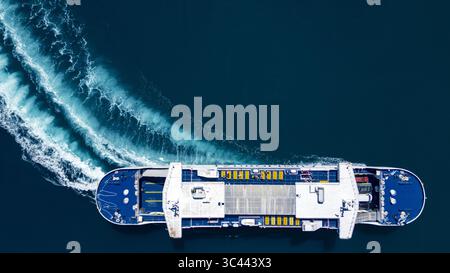 Split, Croatia - 13 July 2024: Aerial view of a large passenger ferry cutting through the deep blue Adriatic Sea, leaving a frothy white wake in its path. Stock Photo