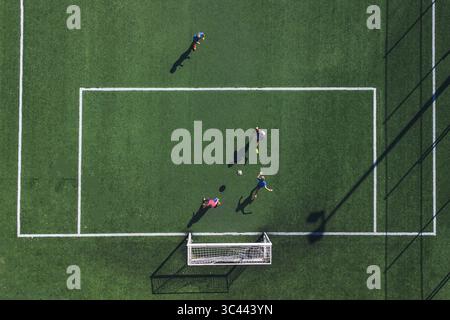 Aerial view of figures playing soccer on a vibrant green field with stark white lines and goalposts, a lively contrast captured from above, Split, Split-Dalmatia County, Croatia. Stock Photo