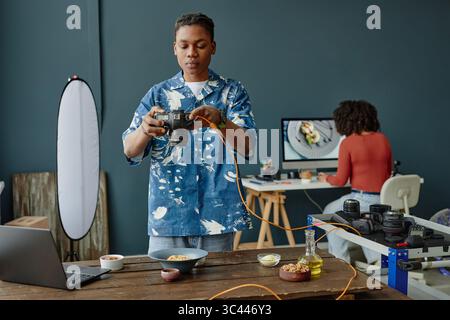 Young Adult Black Man Adjusting Camera While Photographing Food in Studio Stock Photo