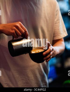 Close-up of a barista hands creating latte art in a coffee cup. Professional coffee preparation captured in a cozy cafe environment, highlighting the Stock Photo
