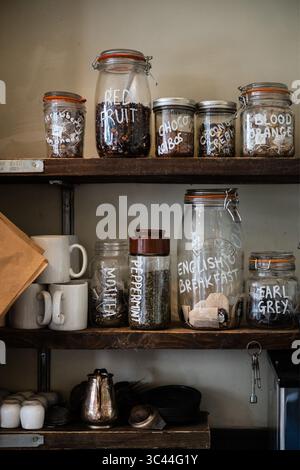 Close-up of rustic wooden kitchen shelves filled with glass jars labeled with different types of loose leaf tea, including peppermint, Earl Grey, red Stock Photo