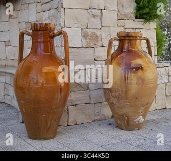 Two rustic terracotta jars stand side by side in front of a traditional stone wall, evoking Southern Italian charm. Stock Photo