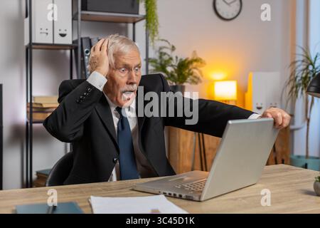 Frustrated senior businessman having software problems with laptop angry grandpa nervous seeing error, mistake notification at computer screen mad employee experience virus attack or app malfunction. Stock Photo