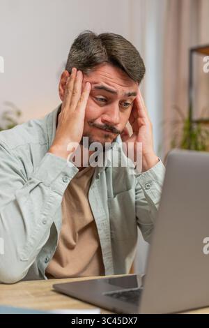 Angry furious man freelancer using laptop while working at home office having nervous breakdown at work, stress management, mental distress problems, losing temper, reaction on failure. Vertical. Stock Photo