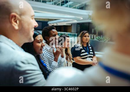 A diverse group of corporate colleagues is seen interacting enthusiastically in a modern office setting. They appear engaged and positive, reflecting Stock Photo