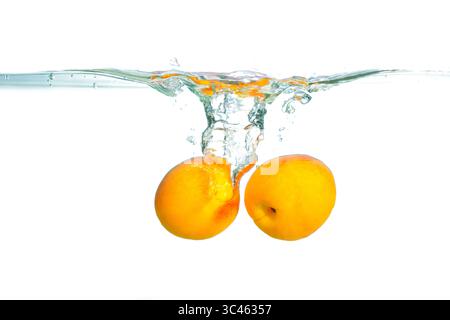 Close-up view of vibrant apricots submerged in clear water, creating lively splashes and ripples around the fruit, emphasizing freshness and vitality. Stock Photo