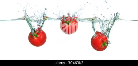 Bright red tomatoes splashing into clear water, creating a dynamic and refreshing scene against a white background. Stock Photo