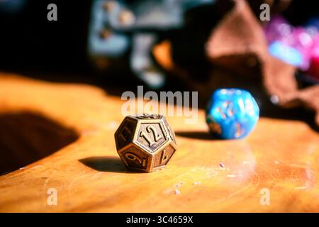 A metallic D12 die and a blue die rest on a wooden table, surrounded by leather pouches. Stock Photo