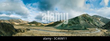 View of rugged mountains painted with hues of green and brown under a vast sky crossed by fluffy clouds in Landmannalaugar, Rangárþing ytra, Iceland. Stock Photo